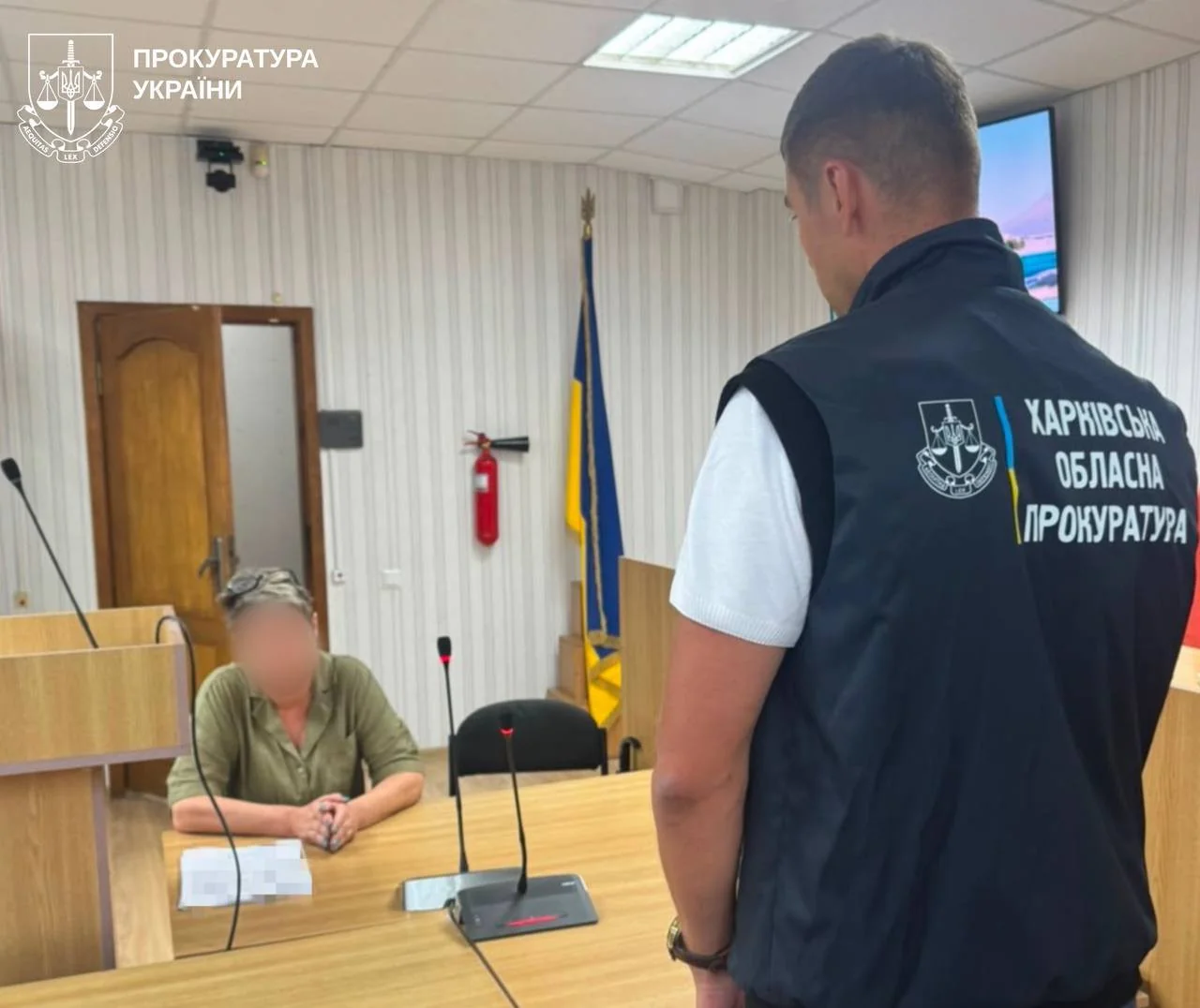 Працівник Харківської обласної прокуратури стоїть біля жінки з розмитим обличчям за столом у кабінеті