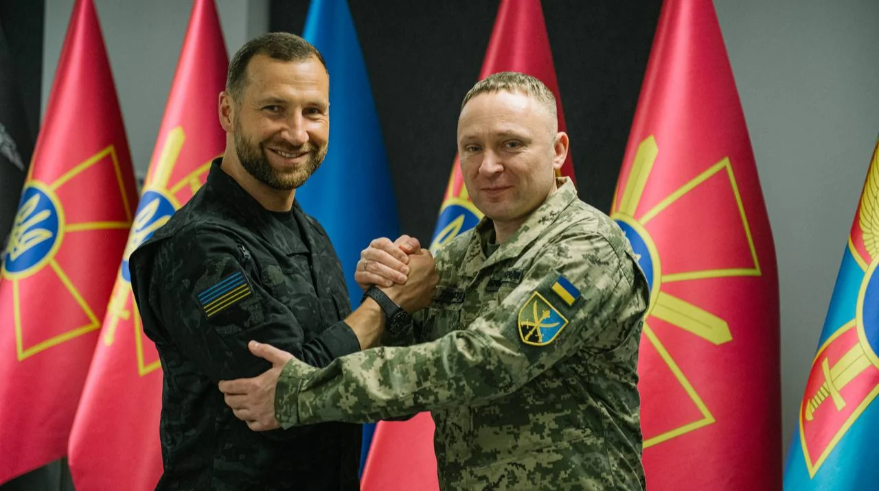Євгеній Хмара тисне руку військовому на тлі українських прапорів