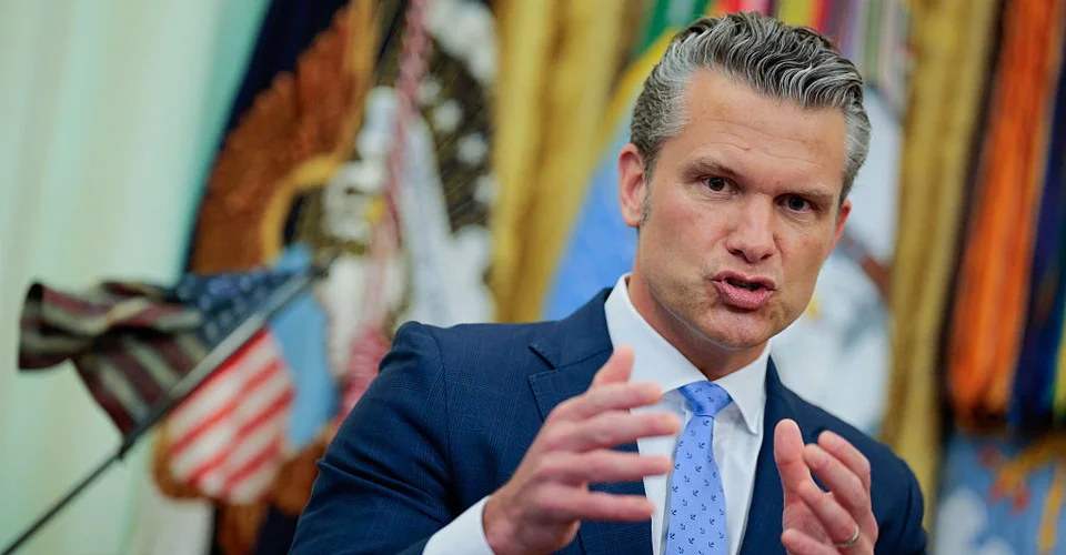 Міністр оборони США Піт Геґсет жестикулює під час виступу на тлі прапорів