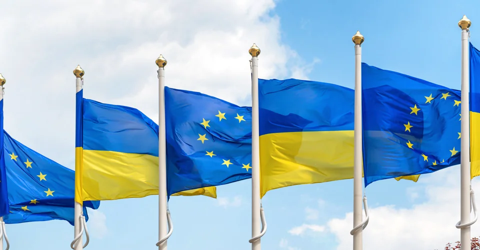 Прапори України та ЄС майорять на флагштоках під блакитним небом